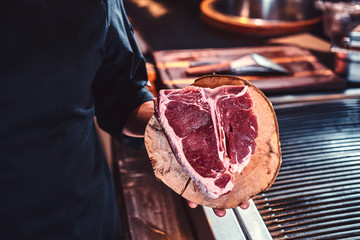 Close-up image of a fresh steak on a wooden cutting board in the hands of a cook.