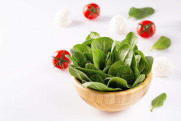 Fresh baby spinach in a wooden bowl on white background.