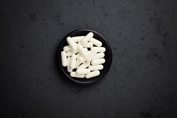 Creatine capsules. Bodybuilding food supplement on black stone background. Top view. Copy space. 