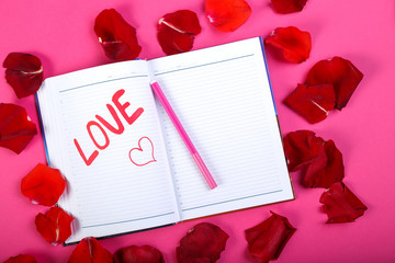 The word love written in red felt-tip pen in a notebook on a pink background in the design of rose petals.
