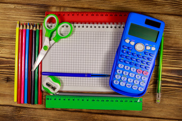 Set of school stationery supplies. Blank notepad, calculator, rulers, pencils, pens, scissors and sharpener on wooden desk. Top view