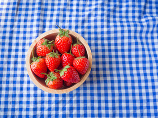 Strawberry in a wooden cup on blue and white checkered fabric texture.