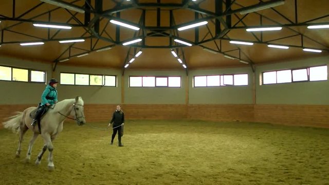 Slow motion kid riding horse indoor. Horse riding instructor helping child learn to ride. Private horse riding lessons.