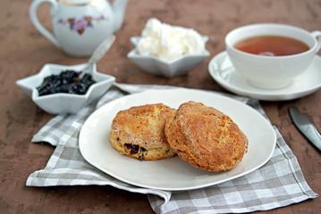 Traditional English scones with dried cranberries on a white plate. Served with jam and whipped cream.