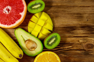 Assortment of tropical fruits on wooden table. Still life with bananas, mango, oranges, avocado,...