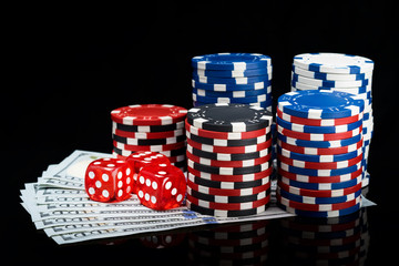 a pack of hundred dollar bills covered with chips and bones for playing poker on a black background