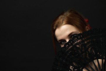 Low Key portrait of seductive young woman hiding face by a crochet black hand fan. All on the dark background.
