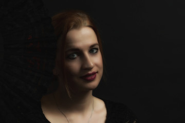 Low Key portrait of seductive young woman holding black fan. All on the dark background.