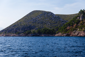 wide, blue sea waters on a sunny day, mountainous and shoreline in the distance; blue sky without clouds