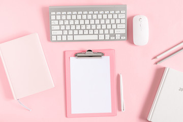 Home office pink table, notepad, clipboard, keyboard, diary, notebook, stationery on pink background. Flat lay, top view, copy space 