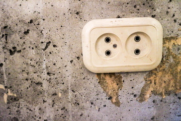 White plastic electric socket on old grey cracked concrete wall 