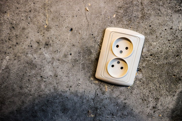 White plastic electric socket on old grey cracked concrete wall 
