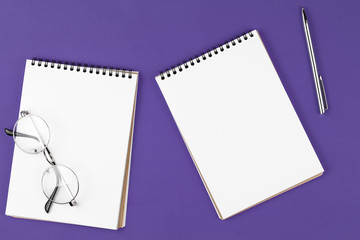 open notebook with pen and glasses on the violet background