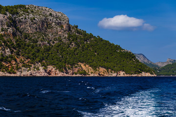 Obraz premium sunny day, sea view to the coast; view of the white waves left by the motorboat; on the shore there are large mountains partially overgrown with trees