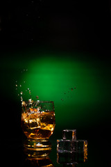 A glass of whiskey on a beautiful green background and a splash from falling ice