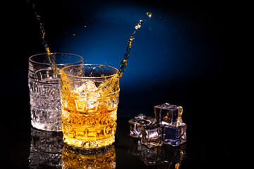 Two crystal glases of whiskey on a beautiful blue background and a splash from falling ice