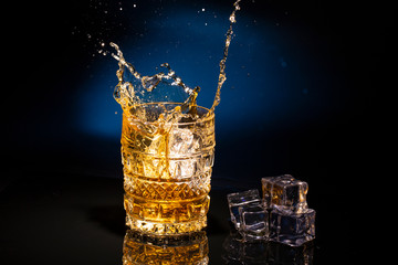 Two crystal glases of whiskey on a beautiful blue background and a splash from falling ice