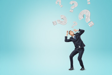 Grey question marks falling on a businessman on blue background
