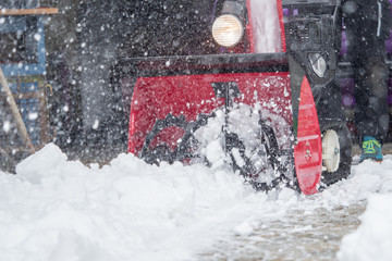 Someone uses a snowthrower outdoors in winter while it is snowing