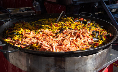 Street food in France, fresh prepared paella with rice and sea food in big pan on street market, ready to eat