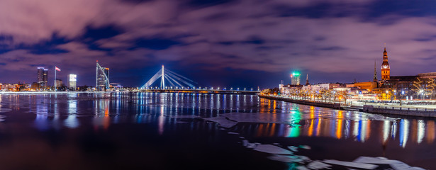 Fototapeta na wymiar Panoramic Cityscape of Riga, Latvia from Akmens Bridge at Night with Dramatic Sky, with the View of Office Buildings and other Bridges over River Daugava