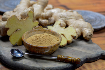 Fresh raw ginger root and bowl with ginger powder close up