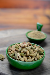 Bowl with cardamom pots and cardamom powder, used for cooking and traditional medicine close up, spices collection