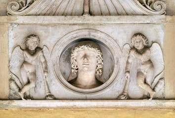 Fototapeta na wymiar Young man of the Colonna family, flanked by a pair of cupids with downturned torches, bass relief in portico of church dei Santi XII Apostoli in Rome, Italy