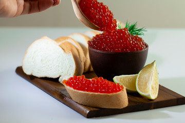 red caviar in a ceramic dish on a wooden platform on a white background