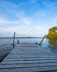 Obraz premium Wooden Bridge on the Side of River with Dramatic Sky and Autumn Color Trees - Free Space for Text, Concept of Travel in Peace and Harmony