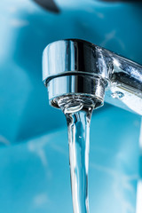 Water flows from a modern chromed water tap faucet macro close-up.
