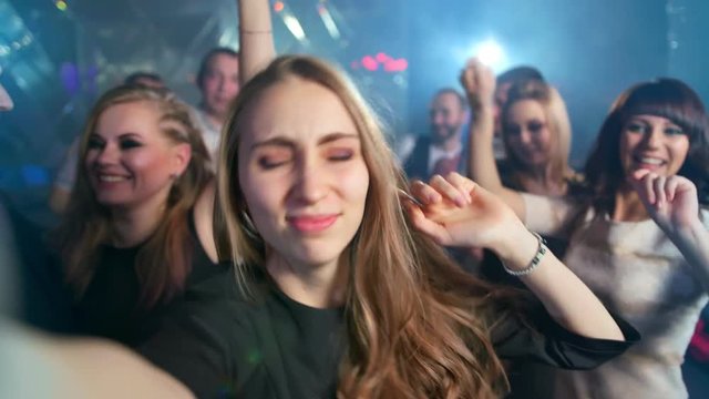 Pretty woman is taking a selfie while dancing at the night club