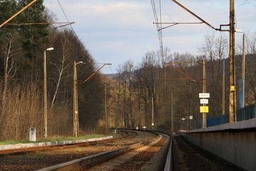 Fototapeta na wymiar Railroad tracks. Railway station, platform in the countryside. A warm, calm, sunny evening in the mountains. The beginning of spring. Waiting for the train. Forest, mountains in the background. 