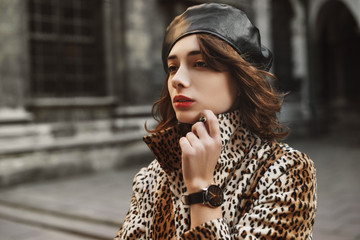 Close up outdoor portrait of young fashionable woman wearing leather beret, black wrist watch, leopard print coat. Copy, empty space for text