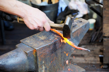 Blacksmith working metal with hammer on the anvil