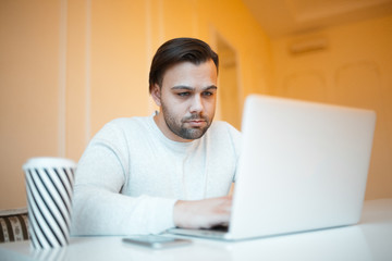 Young man using his laptop, wearing white sweater, over yellow.