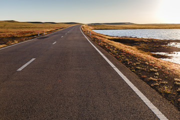 Asphalt road in Mongolian steppe along a small lake