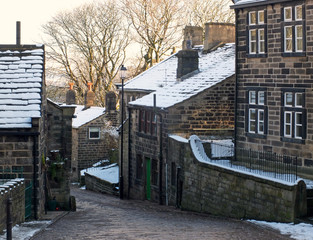 A scenic view of the main street in the village of heptonstall in west yorkshire with snow covering the old stone houses and pennine scenery visible in the background
