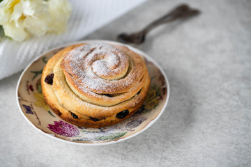 a homemade baked bun with dry fruits on a floral plate, on a grey marble backdrop