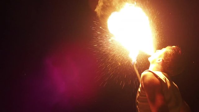 Extreme fire-breathing scene. Guy spit on the fire. Entertaining event on the beach, traveling concept, acrobatics fireshow program for guests. Caucasian man holding flaming stick and breathe fuel
