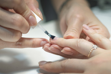 Manicurist is applying a nail base gel on a female finger nails. Nail care concept.