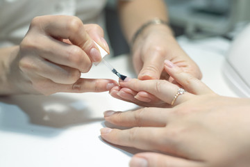 Manicurist is applying a nail base gel on a female finger nails. Nail care concept.