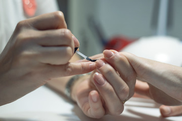 Manicurist is applying a nail base gel on a female finger nails. Nail care concept.