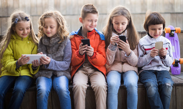 Children Playing With The Phone On Bench Outdoors