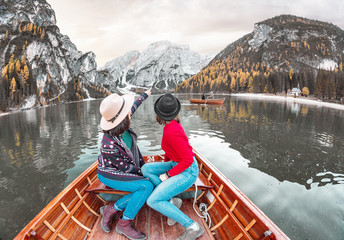 Two happy woman friends on the boat or canoe cruise tour on lago Di Braies lake in Italian...