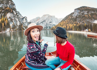 Two happy woman friends pointing to the map on the boat or canoe cruise tour on lago Di Braies lake...