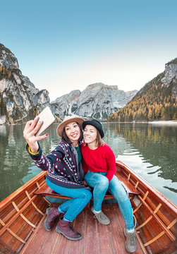 Two happy woman friends making selfie photo on the boat or canoe cruise tour on lago Di Braies lake in Italian Dolomites Alps