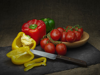 Sweet peppers and red tomatoes, still life. Light painting. With retro knife and slate rustic background.