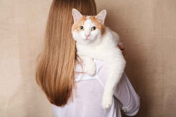 Gentle white cat on a woman's shoulder. White cat on the shoulder of a blonde on a beige background