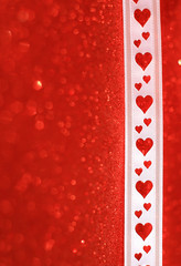 Close up of a white heart patterned ribbon on a red glittering background